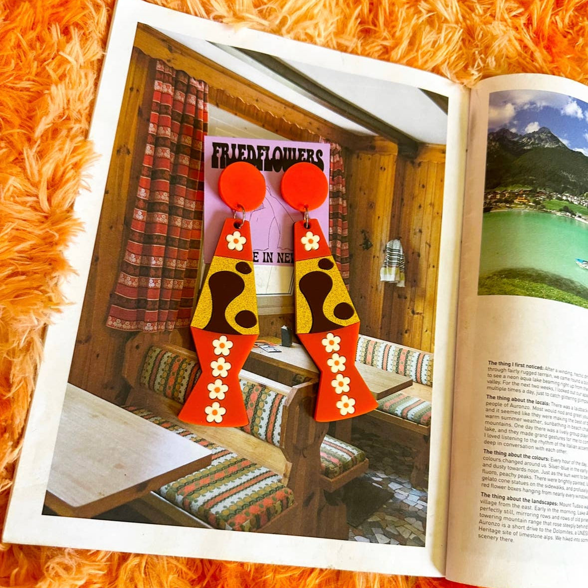 Open magazine on an orange surface with a focus on a pair of earrings.